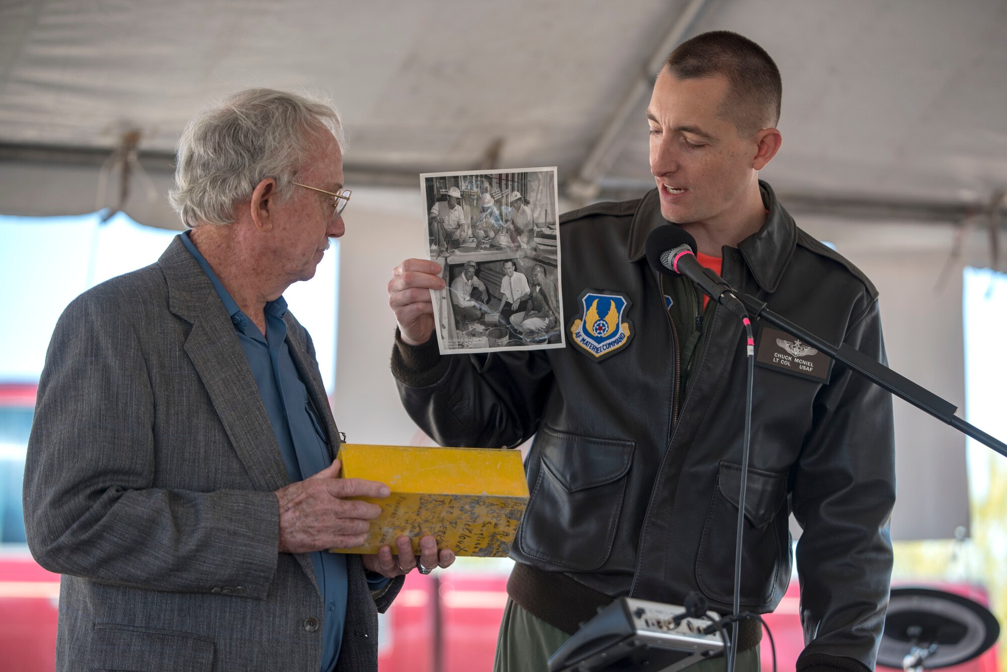 Lt. Col. Charles McNiel, 746th Test Squadron commander, shows a photo of Grady Nicholson, a former 46th Test Group engineer, during a 746th TS 60th anniversary event, Oct. 25, 2019, on Holloman Air Force Base, N.M. The photo shows a picture of Nicholson burying the same time capsule they opened for the anniversary event. (U.S. Air Force photo by Staff Sgt. Christine Groening)