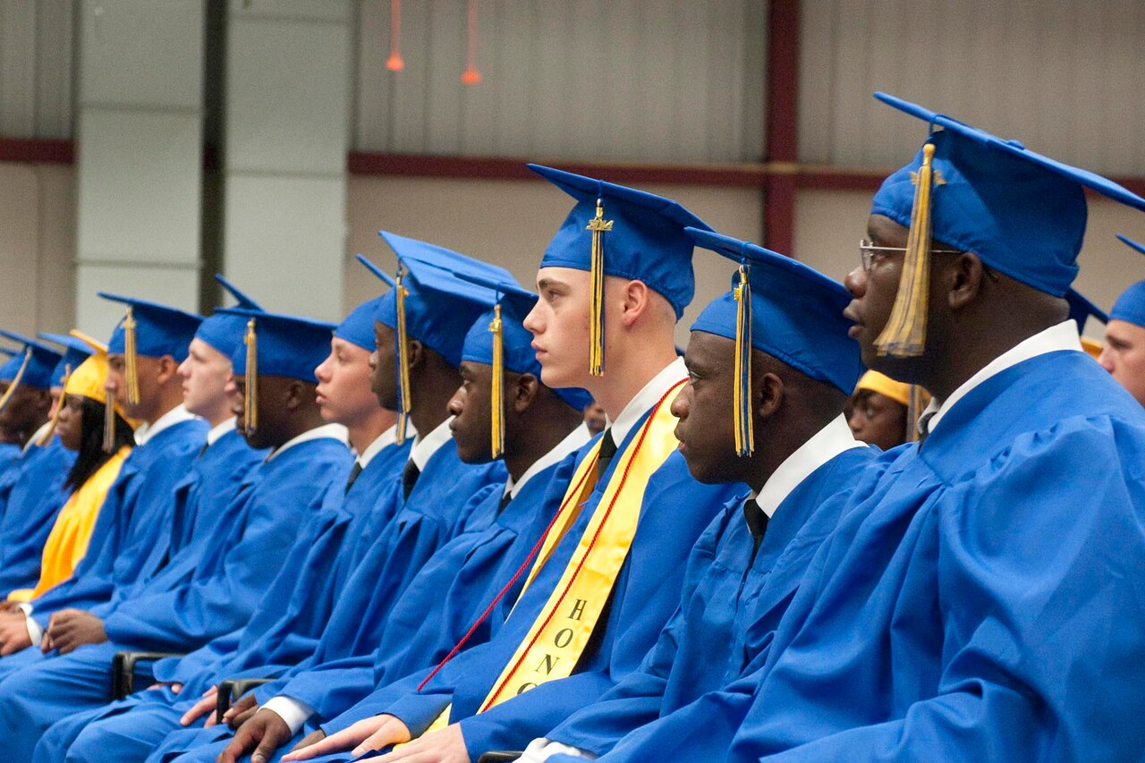 Graduates wearing caps and gowns are seated in a row.