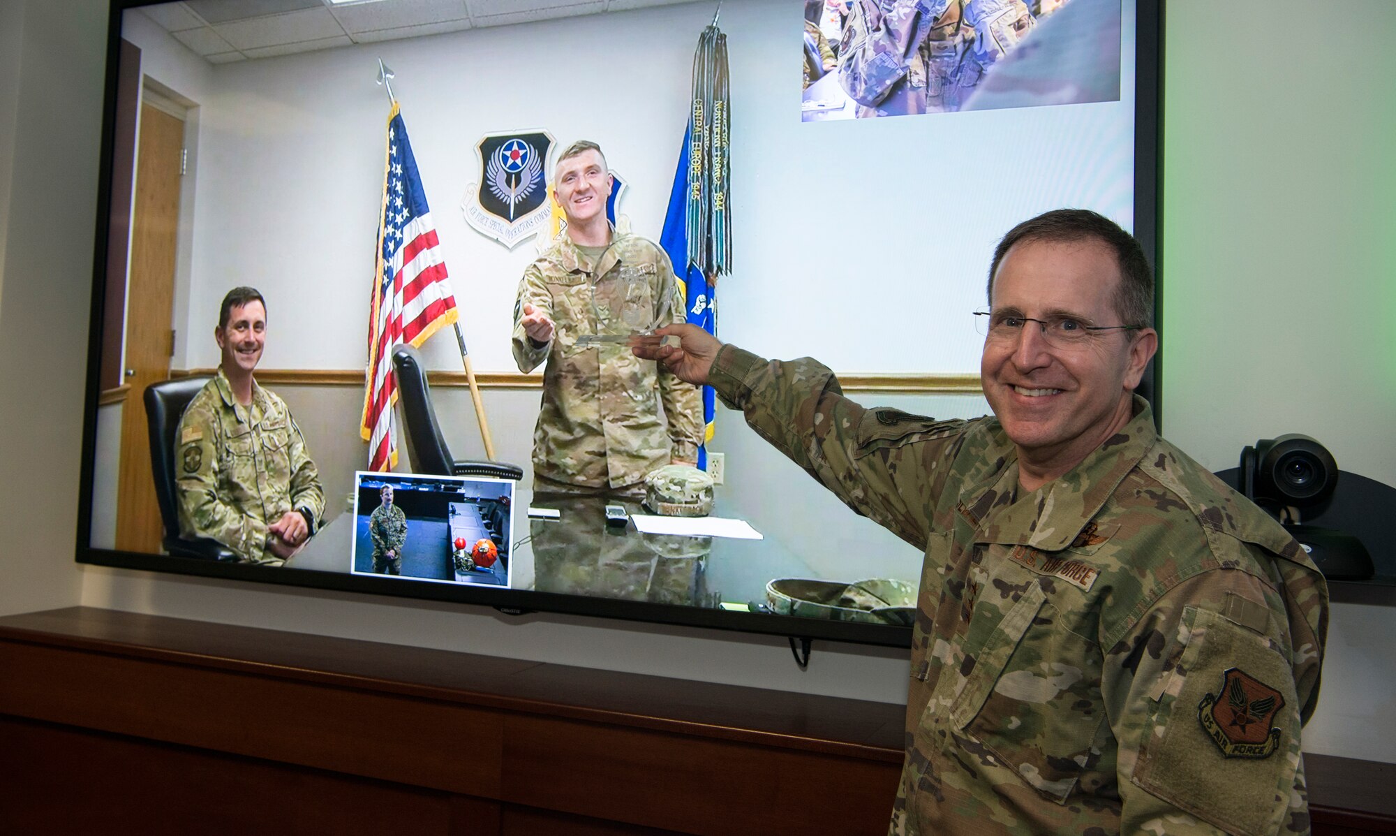 One person presenting an award to someone near a television screen.