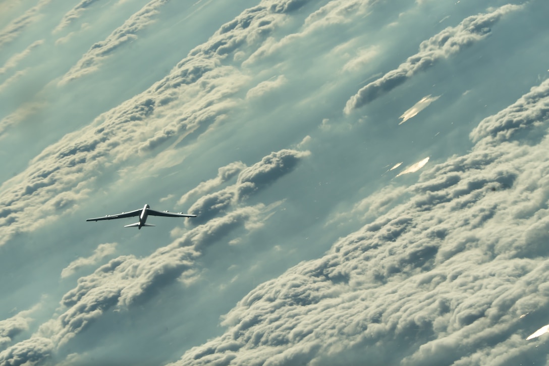 An Air Force bomber flies above clouds and blue sky.