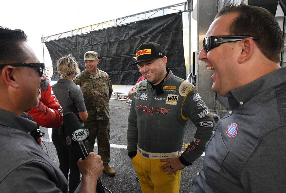 The National Hot Rod Association held their Midwest Nationals at the World Wide Technology Raceway at Gateway Motorsports, Madison Illinois recently.  In background, Lt. Col. William McLeod, 932nd Maintenance Group commander, waits to enter the stage as Fox Sports interviews race car driver Ritchie Crampton.  Col. McLeod was invited to help start the event as an honored guest, Sept. 29, 2019.  McLeod was brought on stage during the opening ceremony and presented an NHRA challenge coin as he waved to the cheering crowd.  (U.S. Air Force photo by Lt. Col. Stan Paregien)