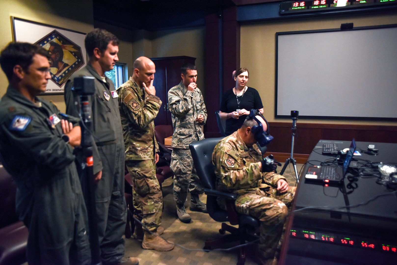 Members of AFWERX and the 189th Airlift Wing Innovation Team watch as Col. Dean Martin, 189th AW commander, tests the virtual reality headset and haptic glove designed to streamline training.