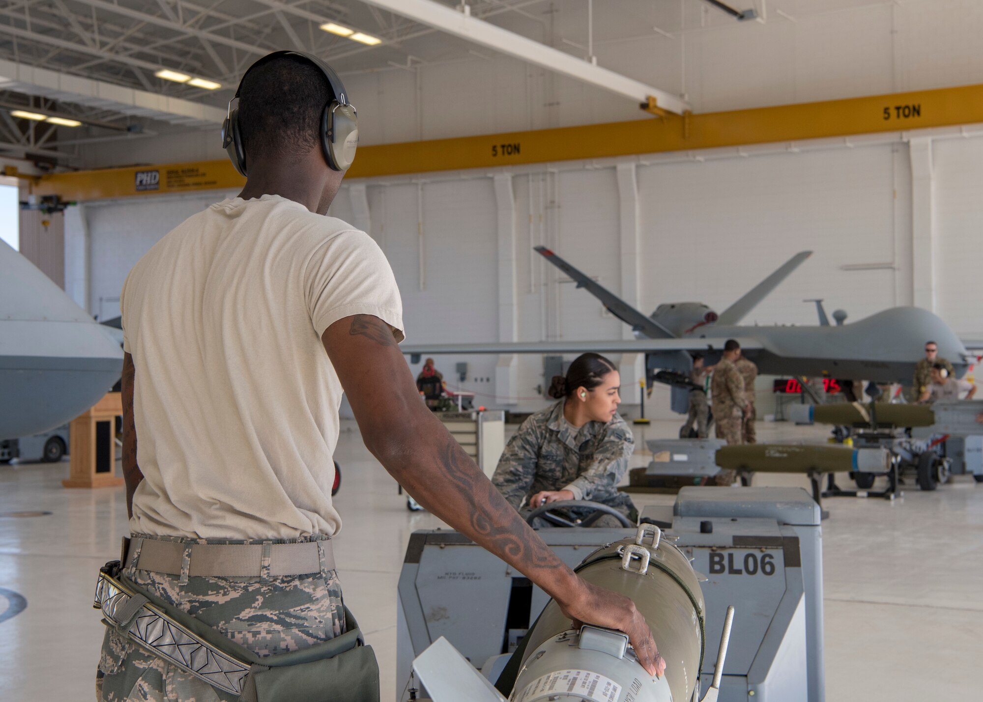 Staff Sgt. Kendrick Johnson, 9th Aircraft Maintenance Unit weapons load crew chief, steadies an inert bomb while Airman 1st Class Jocilyn Rodriguez, 9th Aircraft Maintenance Unit weapons load crew member, directs it to be loaded on an MQ-9 Reaper, Oct. 28, 2019, on Holloman Air Force Base, N.M. Two F-16 Vipers and two MQ-9 Reapers were used to test the loading skills of 12 Airmen during the 2019 third quarter load competition. (U.S. Air Force photo by Airman 1st Class Autumn Vogt)