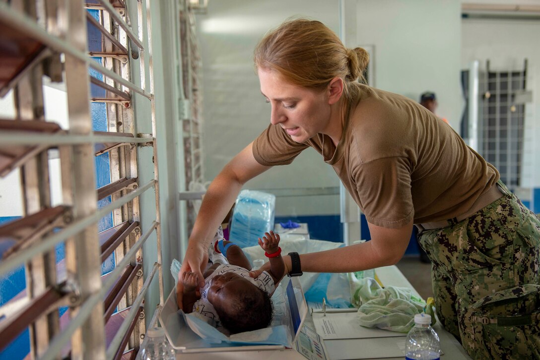 A Navy nurse holds a baby on a scale.