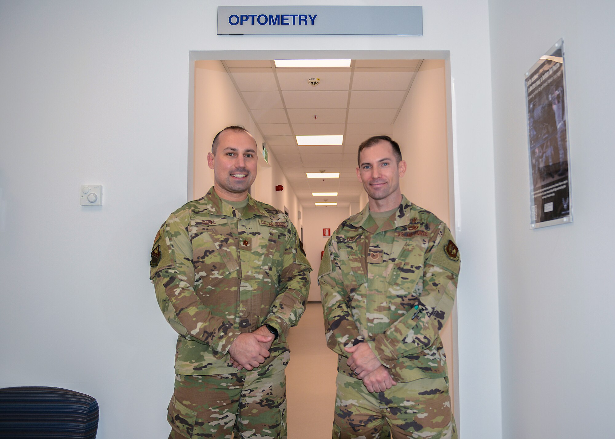 U.S. Air Force Maj. Matthew Tholl, 31st Aerospace Medicine Squadron optometry flight commander (left) and U.S. Air Force Tech. Sgt. Joel Ives, 31st Aerospace Medicine Squadron optometry flight chief (right) pose in front of the entrance of the new Optometry office at Aviano Air Base, Italy, Oct. 30, 2019. Optometry treats up to 25 patients every day. (U.S. Air Force photo by Airman Thomas S. Keisler IV)