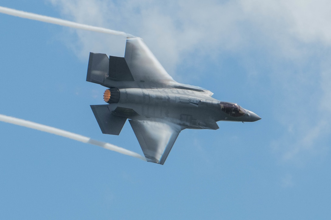 A military fighter aircraft flies across a blue sky.