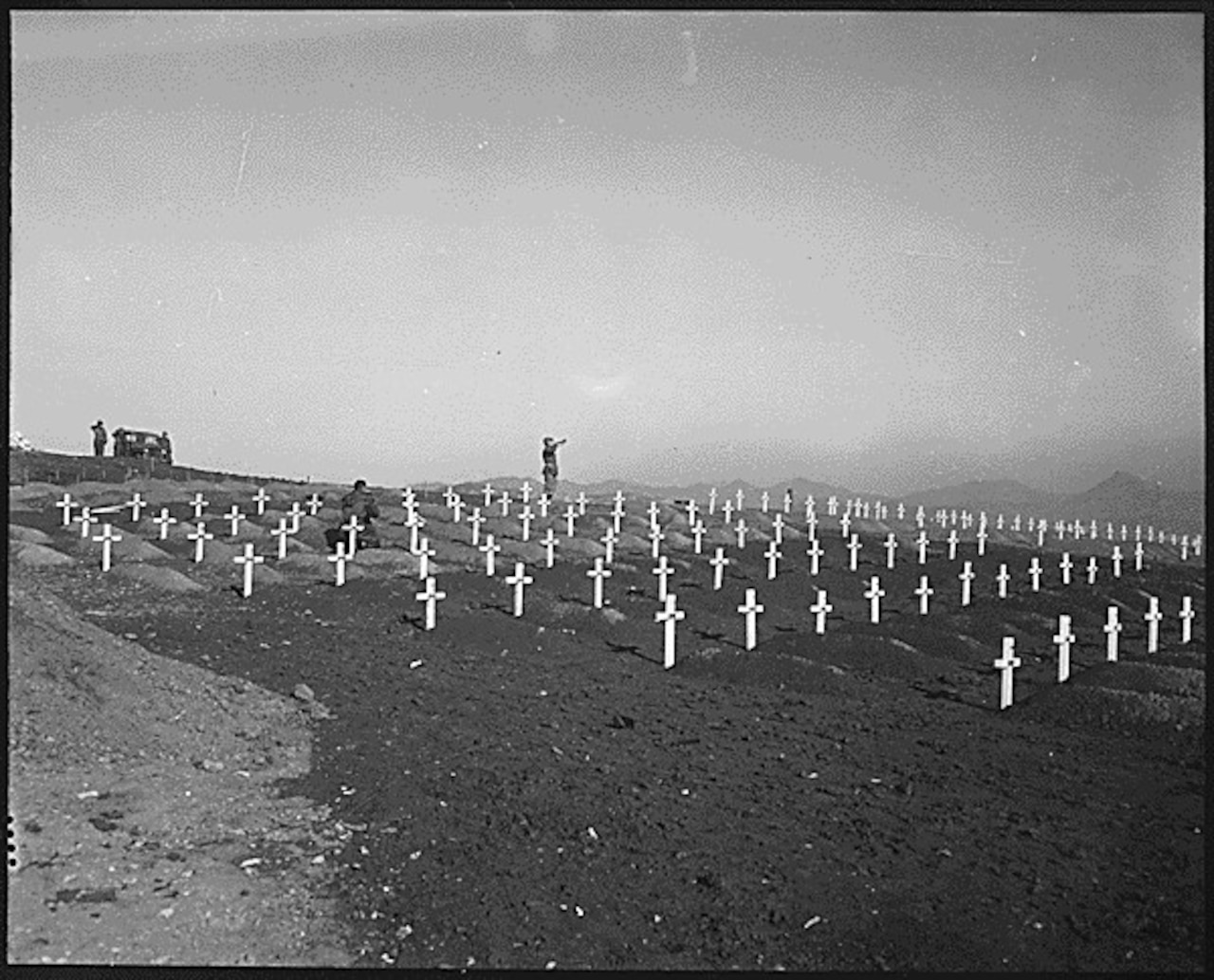 A bugler stands in the distance blowing his bugle in the direction of several rows of crosses at freshly dug graves.
