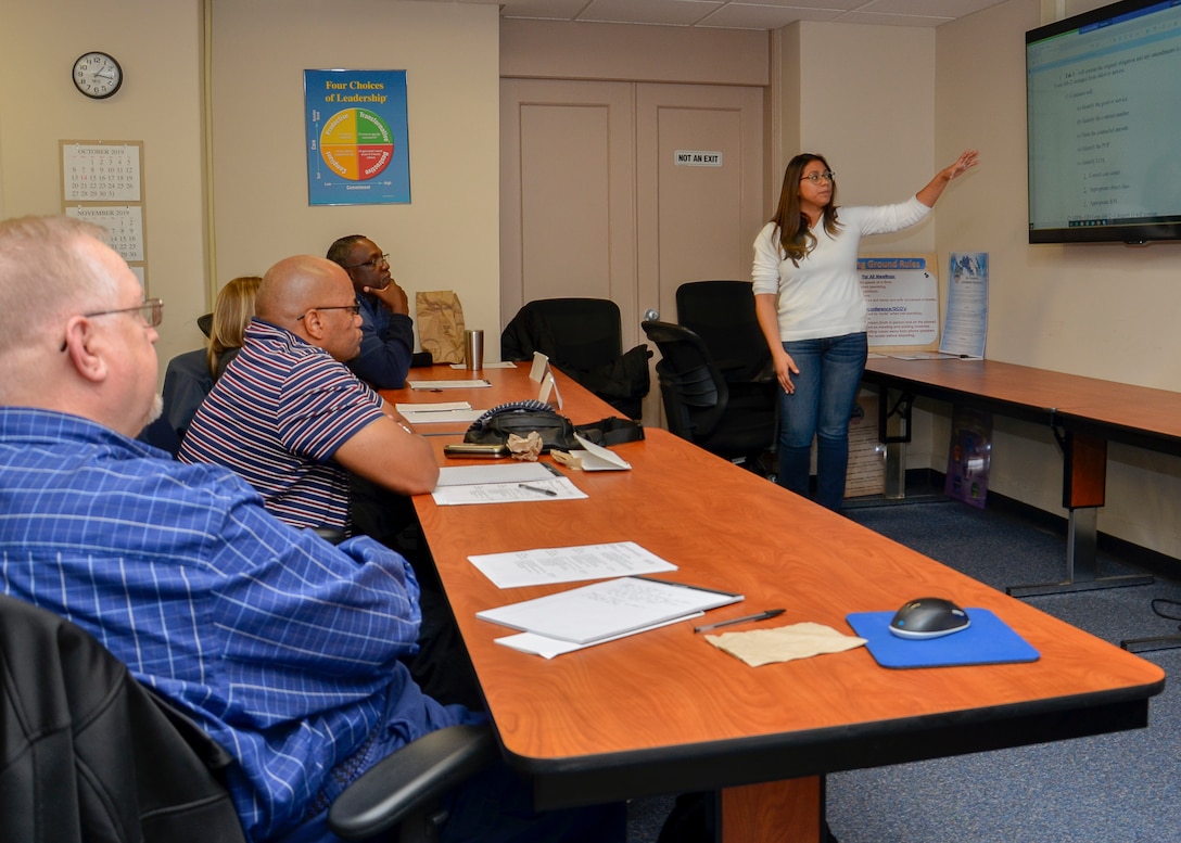 Crystal Leija stands in front of a group of people sitting at tables and leads a workshop topic.
