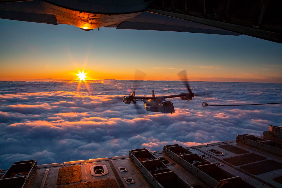 A plane flies over clouds with the sun in the background.