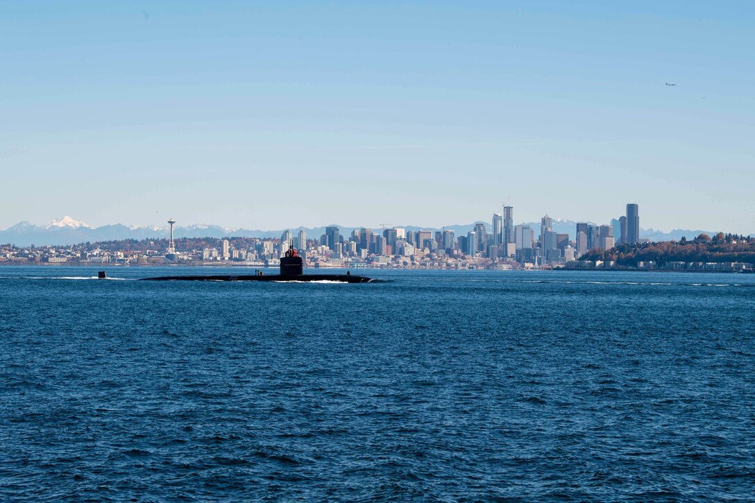 A submarine moves through waters with a city skyline in the background.