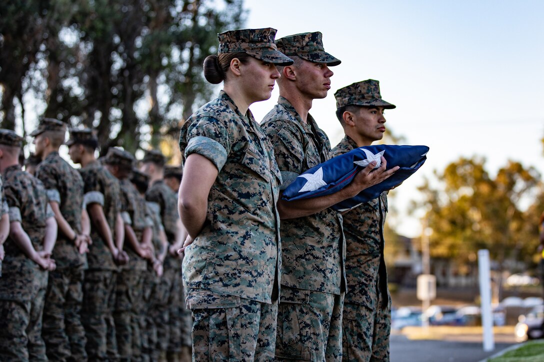 Marines stand in formation as one of them holds a folded American flag.