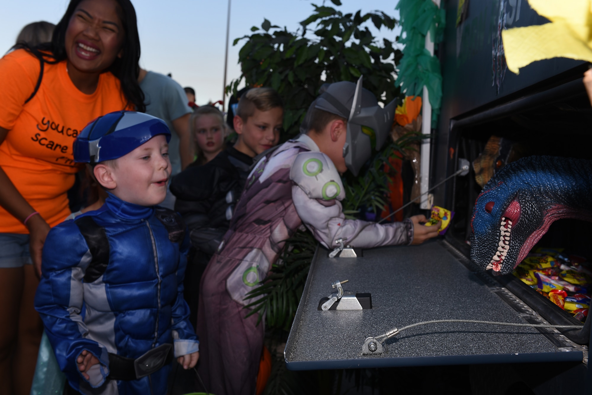 Kids grab candy from dinosaur hand puppets during the Trunk-or-Treat event Oct. 25, 2019, at Travis Air Force Base, California. The Airman and Family Readiness Center hosted Trunk-or-Treat, an annual event aimed to provide a safe place for military families to enjoy Halloween festivities. The event had approximately 5,000 attendees and more than 60 vehicle trunks loaded with candy. (U.S. Air Force photo by Airman 1st Class Cameron Otte)