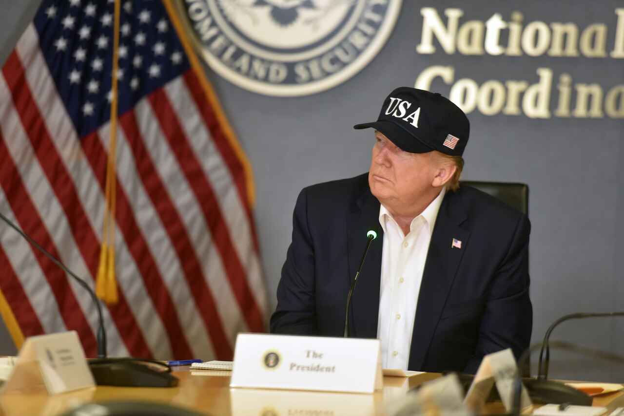President Trump, wearing a black USA baseball cap, listens during a briefing.