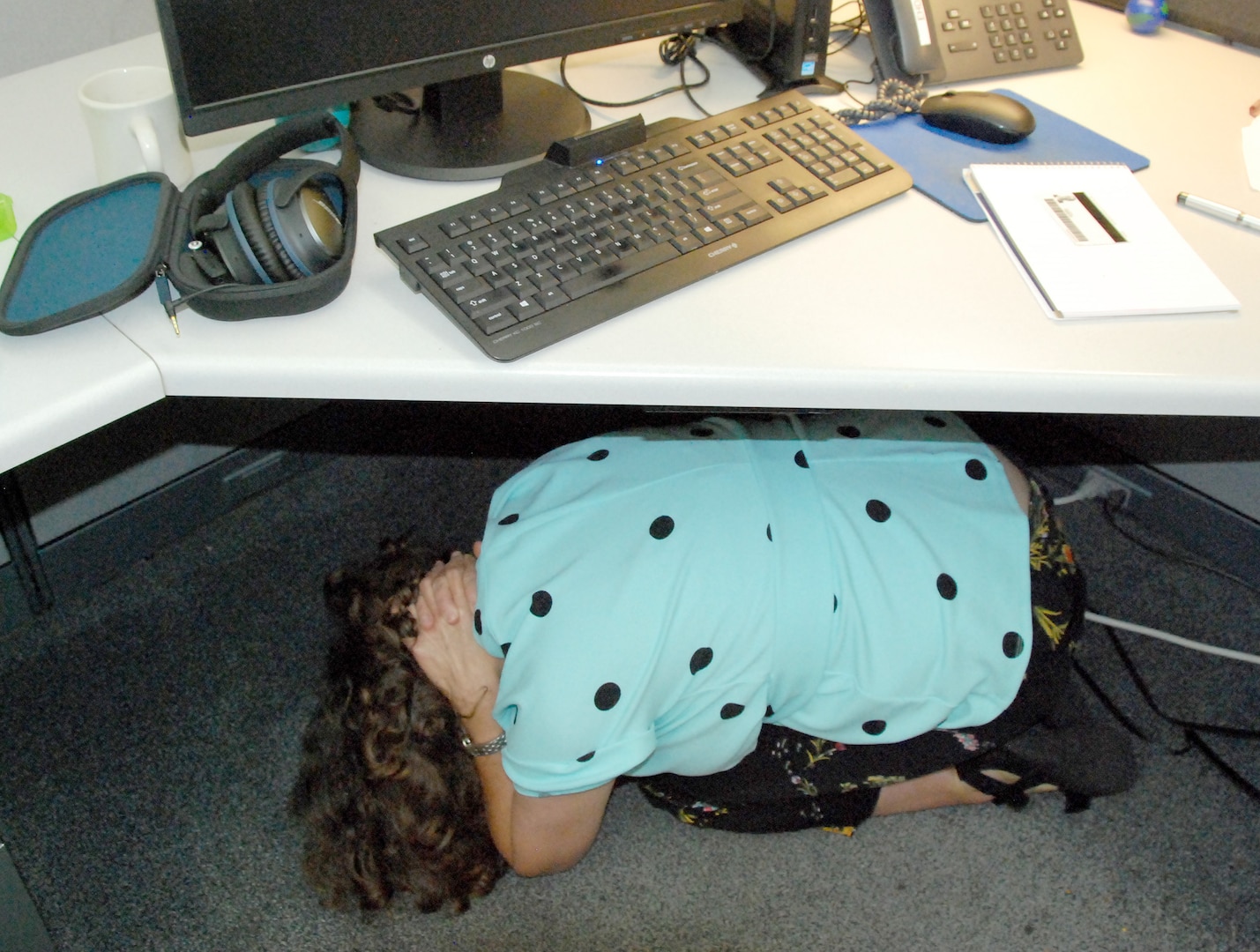 Linda Adams, a management analyst for Defense Logistics Agency Information Operations, demonstrates the “Drop, Cover and Hold On” guidelines for reducing injury and preventing death during earthquakes by curling up under her desk and placing her hands on the back of her neck. Photo by Beth Reece