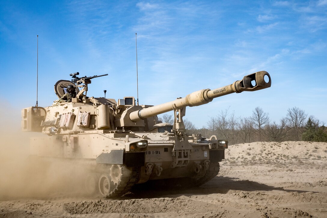 Paladin howitzer travels on dirt road kicking up a trail of dust.