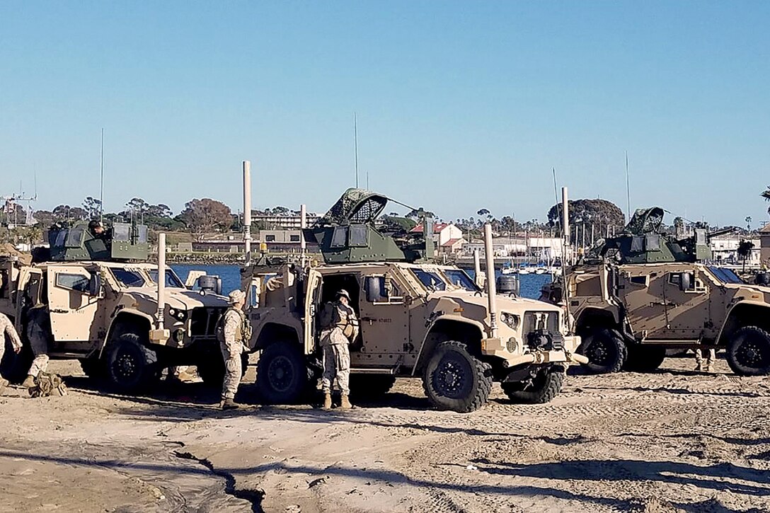 Long shot image of 3 Humvees with 2 Marines checking over the vehicles.