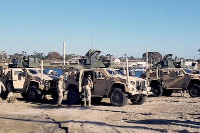 Long shot image of 3 Humvees with 2 Marines checking over the vehicles.
