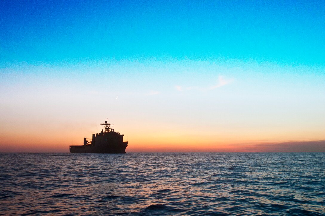 Image of ocean view at sunset on the horizon with USS Fort McHenry in the distance.