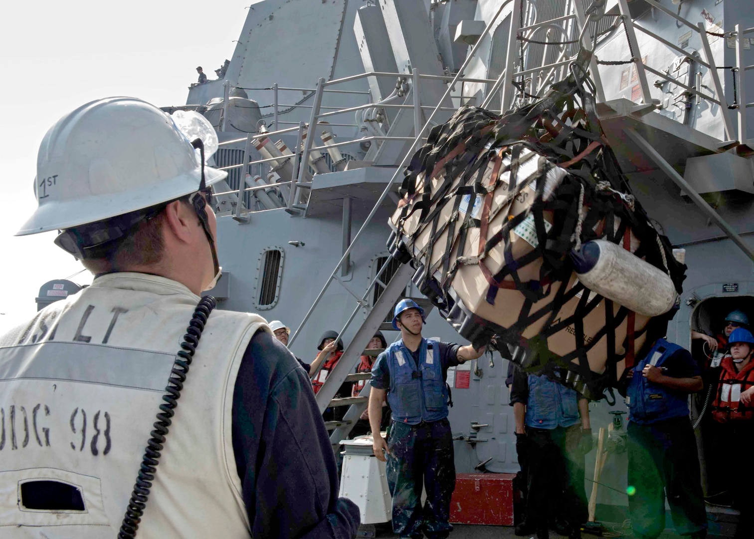 Image of sailors onboard a ship using a hook lift a cargo net of supplies.