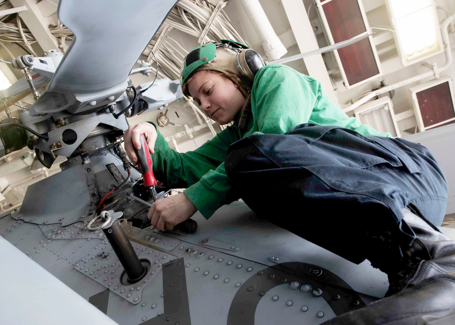 Image of a sailor leaning under stationary helicopter rotor while working on repairs.