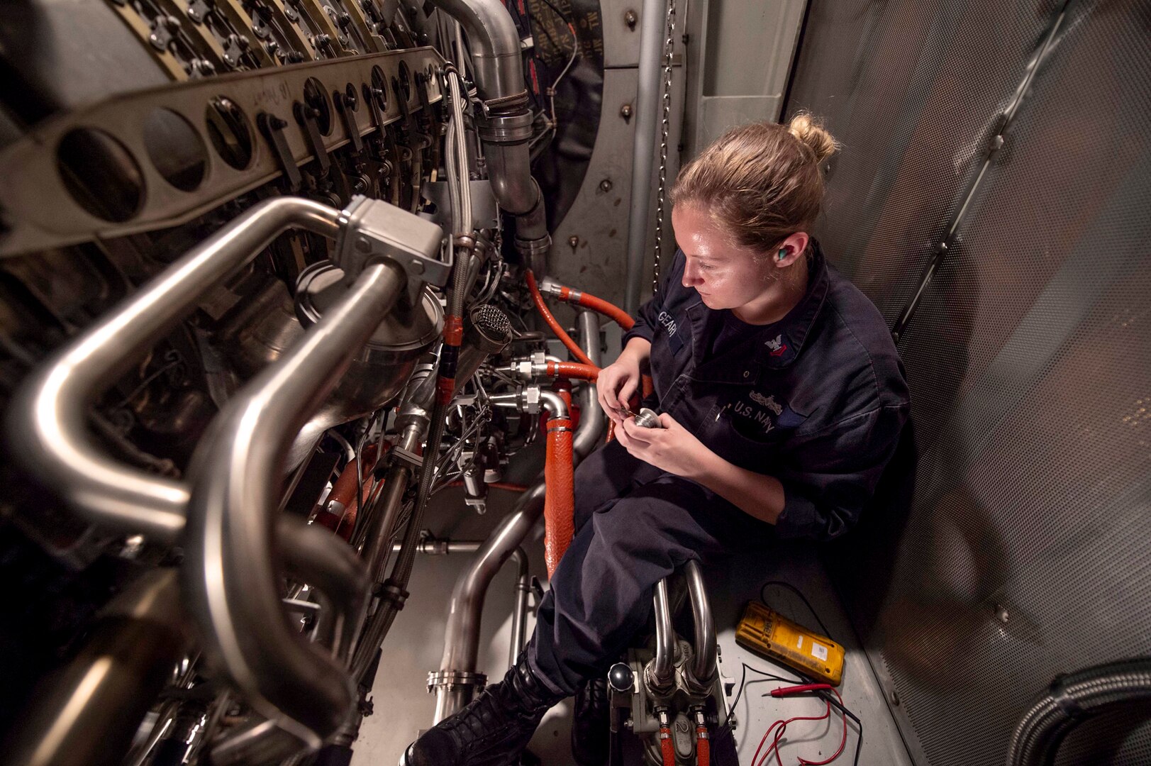 Image of a female sailor inside an engine compartment performing maintenance.