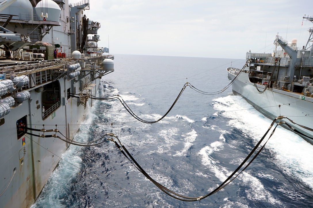 Image of two navy ships at sea with fuel resupply lines running between the two ships.