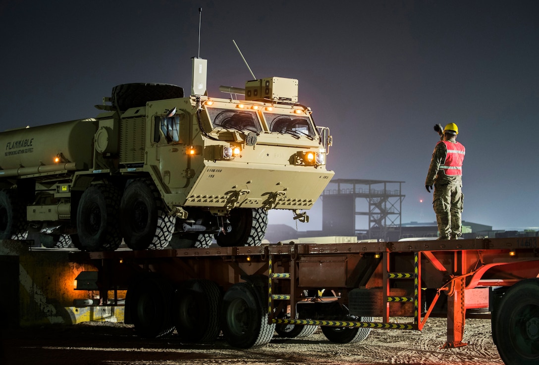 Image of National Guard soldier guiding fuel tanker onto large flatbed transport.