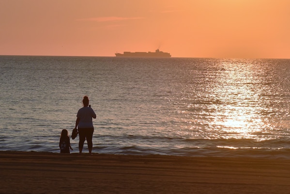 Mother and daughter on the beach watch a ship out in the ocean at sunrise