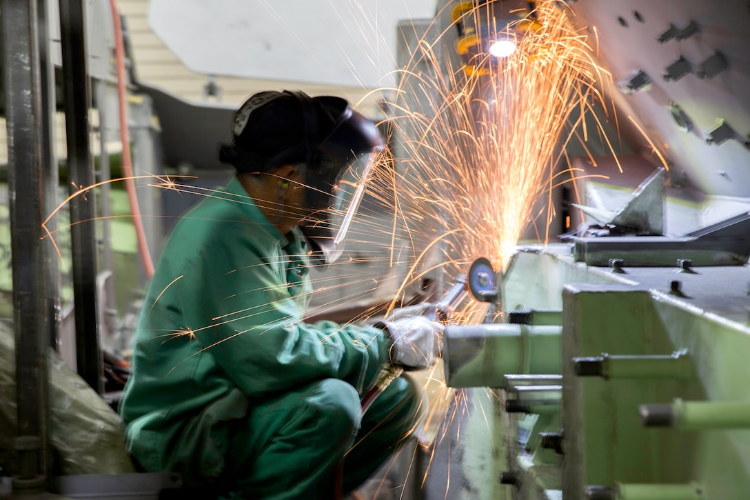 Image of a welder with a angle grinder with sparks coming off the metal plate he's working on.