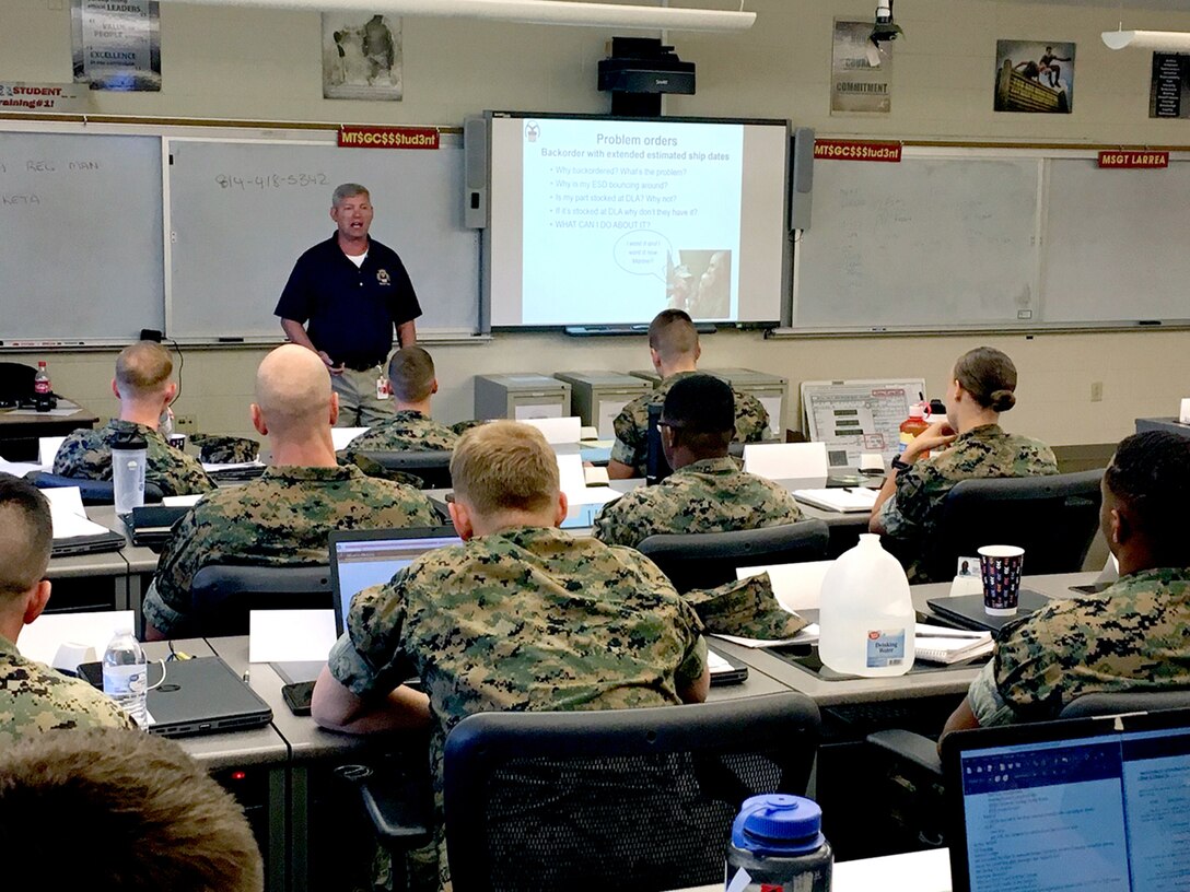 Image of classroom setting with Marines seating at desks and instructor at top left of image.