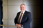 Portrait of Andy Monday standing at a rail at DLA HQC with square block background.