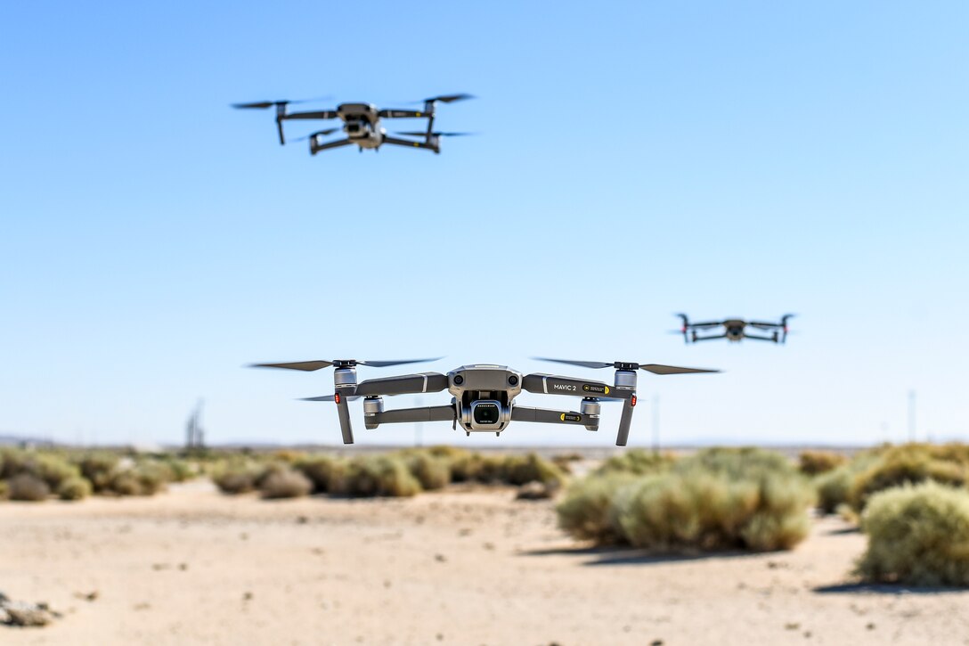 Three drones hover above desert terrain.