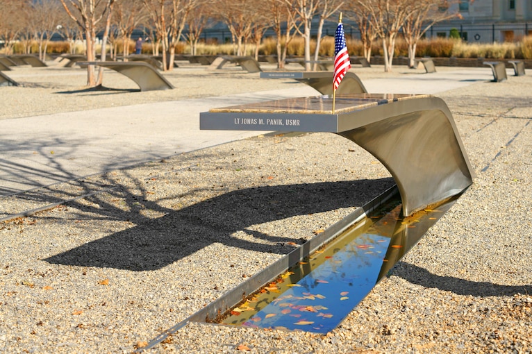 A memorial bench with a name inscribed and a small American flag.