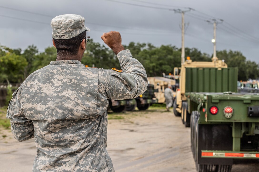A soldier holds up his fist to signal a truck driver out of frame.