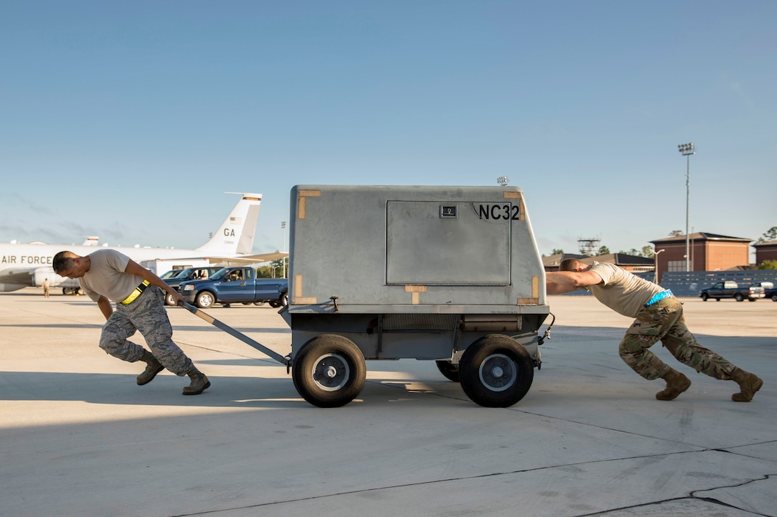 Two airmen push a cart on a runway.