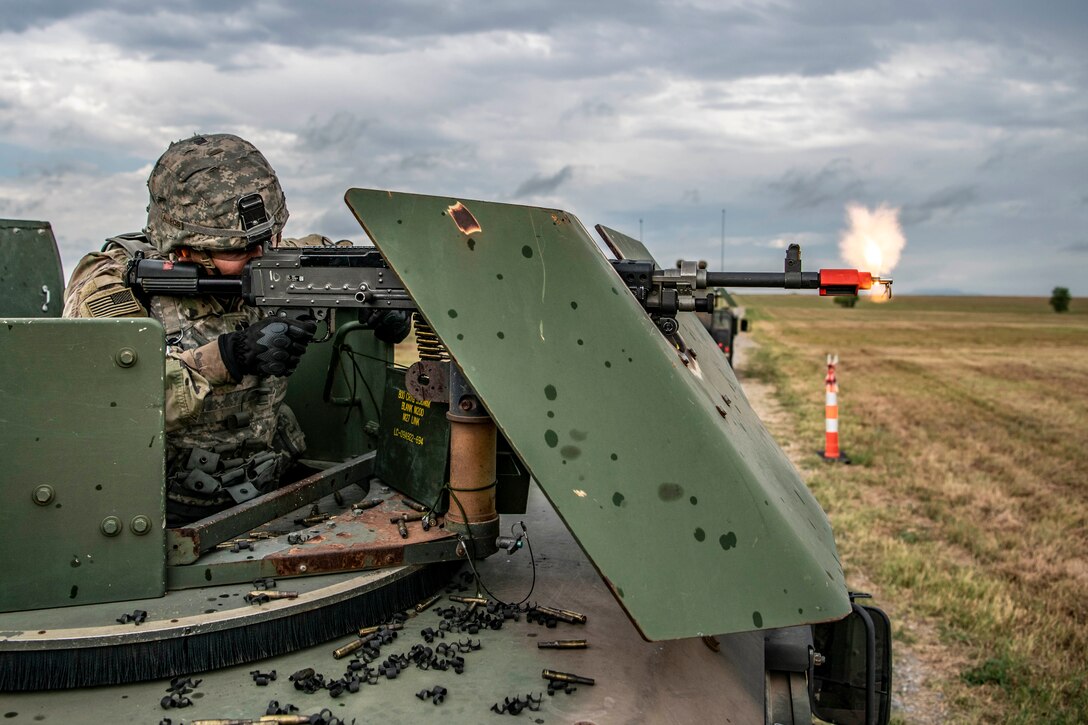 A soldier fires a gun from a military vehicle.