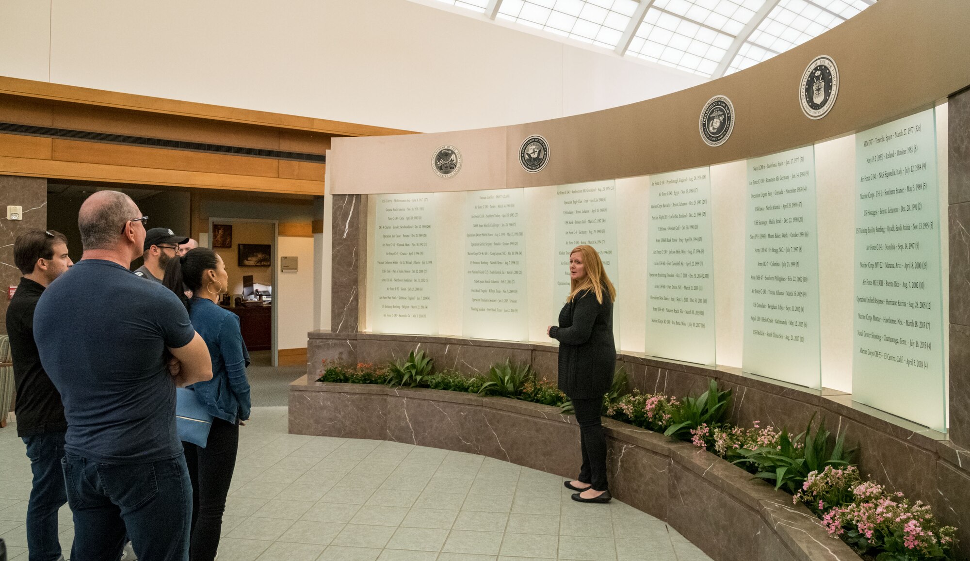 Christin Michaud, Air Force Mortuary Operations Affairs public affairs officer, briefs chef Robert Irvine and his wife, Gail Kim, about the AFMAO memorial wall, Aug. 27, 2019, at Dover Air Force Base, Del. The Memorial Wall represents many of the fallen service members and civilians throughout the years of the mortuary’s history. (U.S. Air Force photo by Roland Balik)