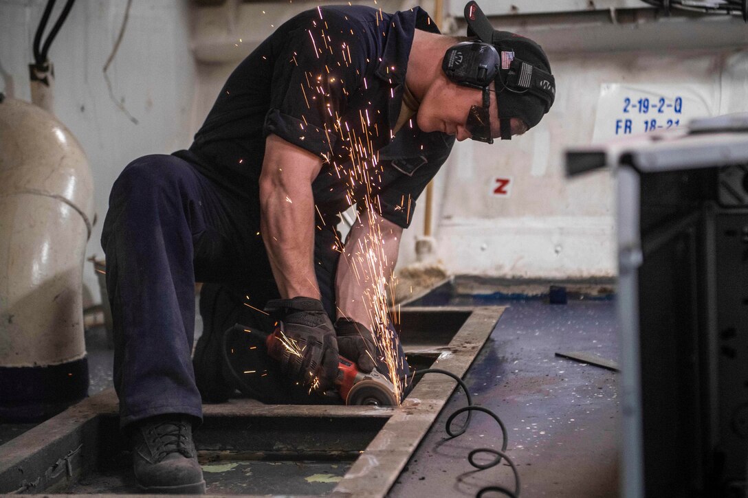 A sailor uses a tool to sand a metal frame.