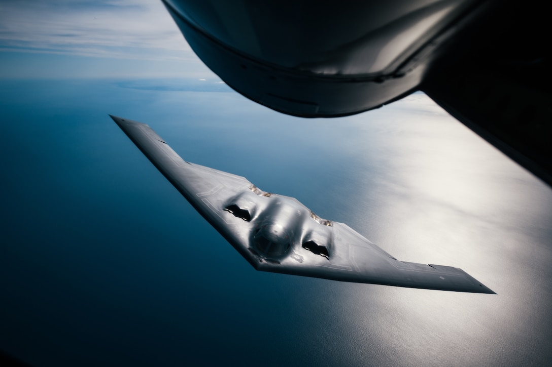 An Air Force B-2 Spirit bomber flies above a dark blue ocean.