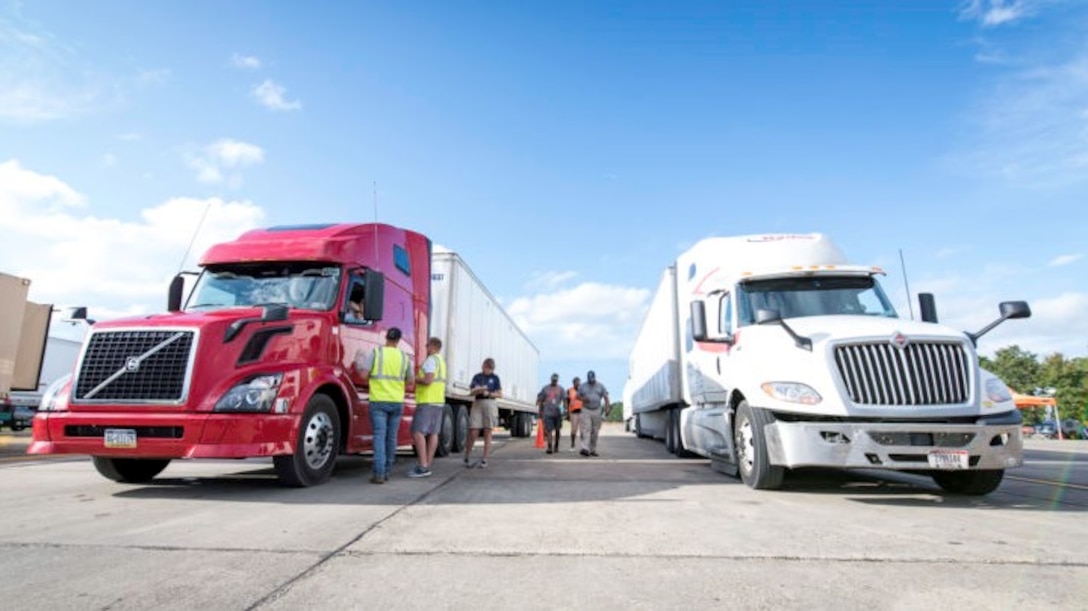Anthony Jones, Ryan Sisson, and Derek Smith, center, work with Federal Emergency Management Agency employees, left, to stage trucks arriving with commercial meals.