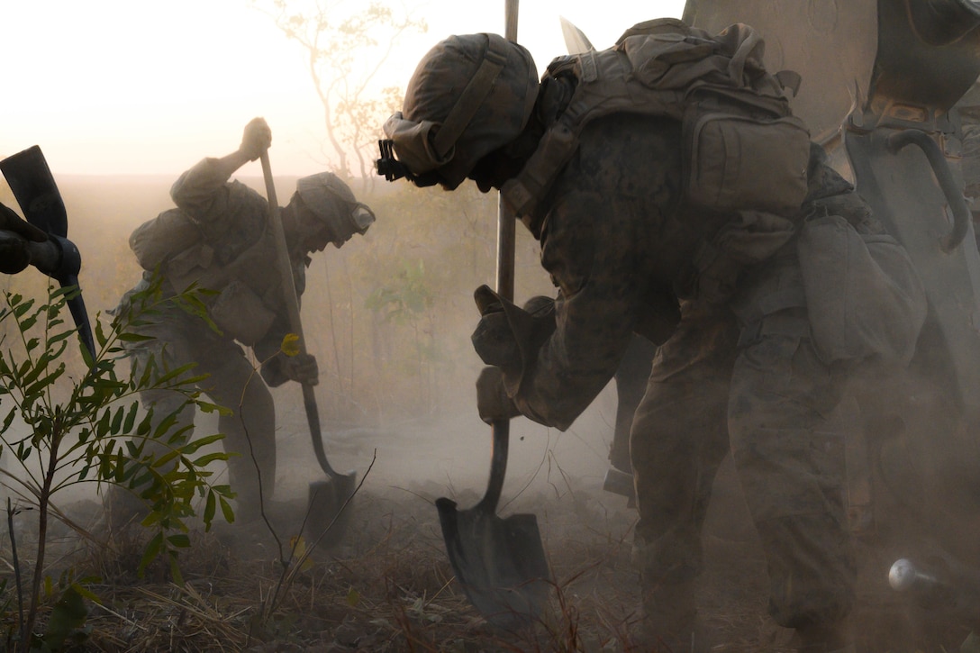 Two Marines use shovels to dig an emplacement.