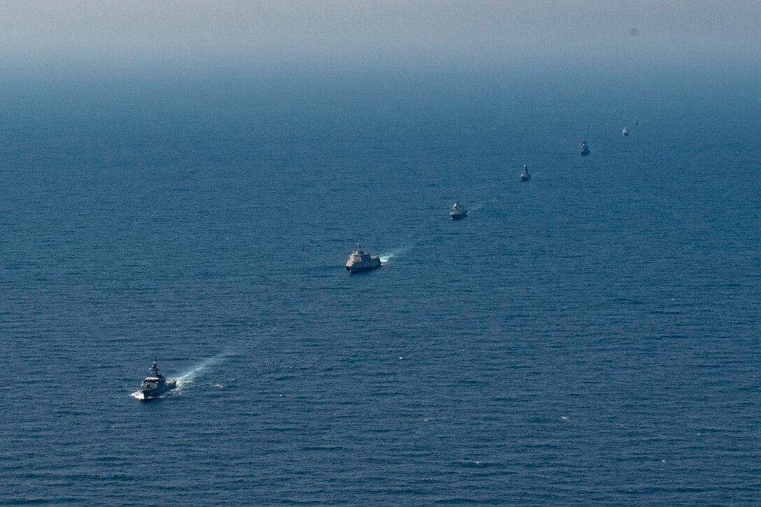 A group of ships sail in a single file line.