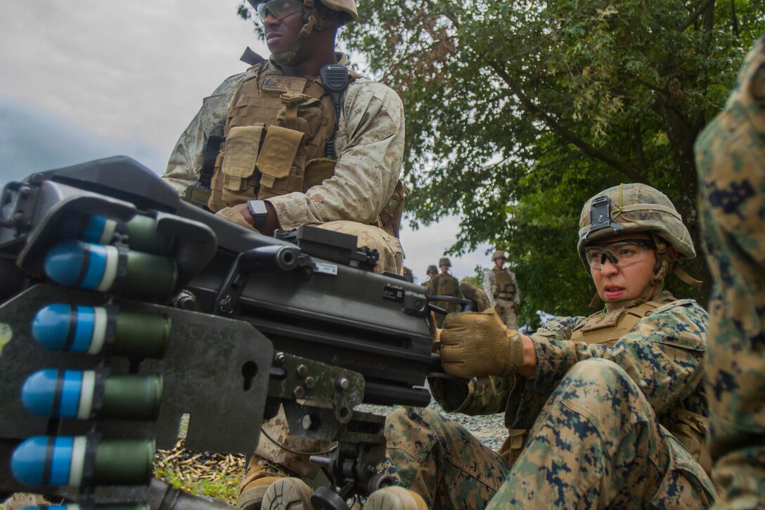 A Marine fires a grenade launcher while seated.