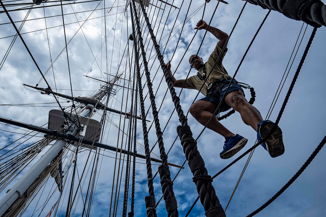 A sailor climbs a mast of a ship.