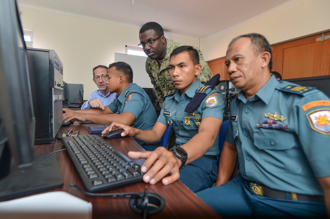 U.S. Navy sailor looks at a computer monitor with sailors from the Indonesian navy.