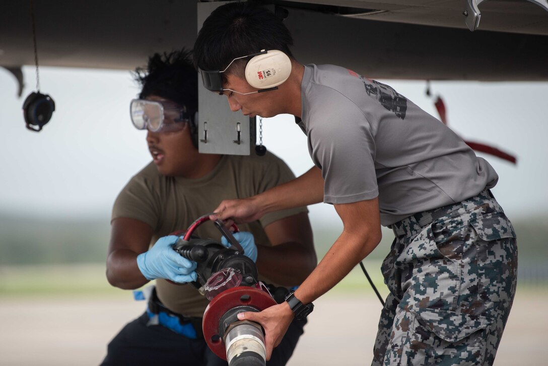 U.S. and Japanese service members work under an aircraft wing.