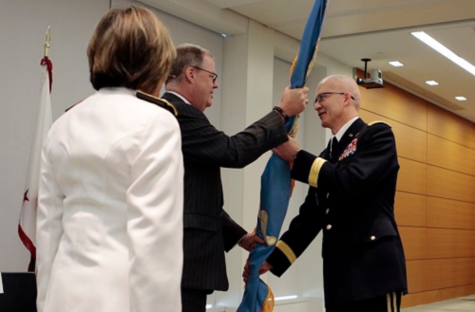 Assistant Secretary of Defense for Health Affairs Tom McCaffery (center), passes the colors to the new DHA director, Army Lt. Gen. Ronald Place (right), as Navy Vice Adm. Raquel Bono, the outgoing director of the Defense Health Agency, watches.