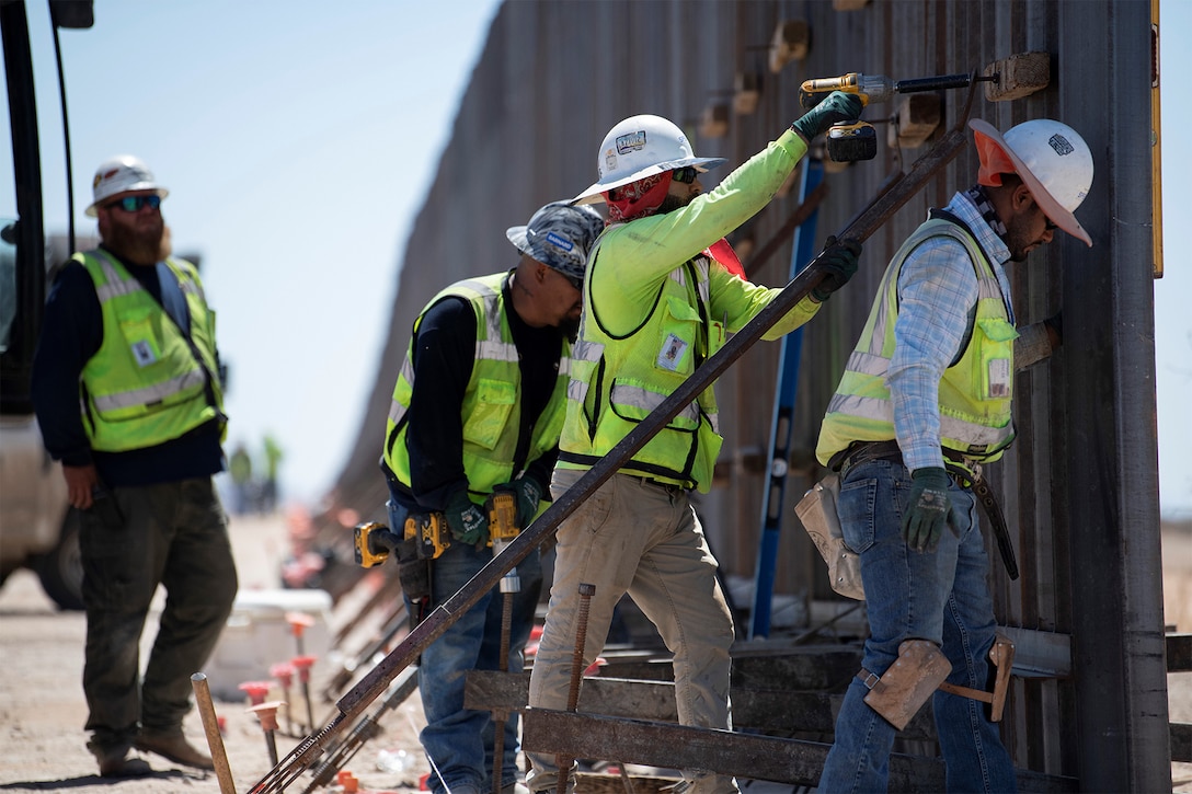 Crew members in personal protective equipment secure braces along a steel wall.