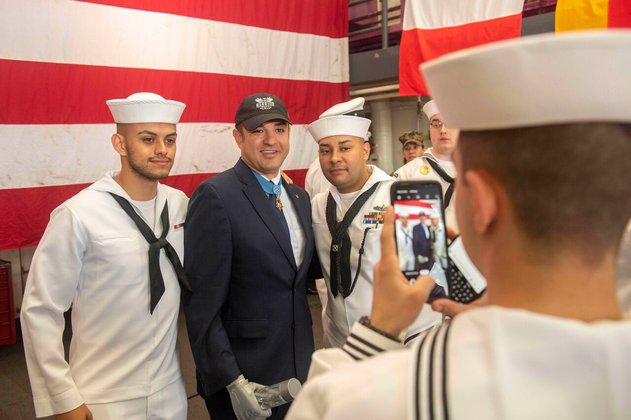 Service members stand in front of a flag.