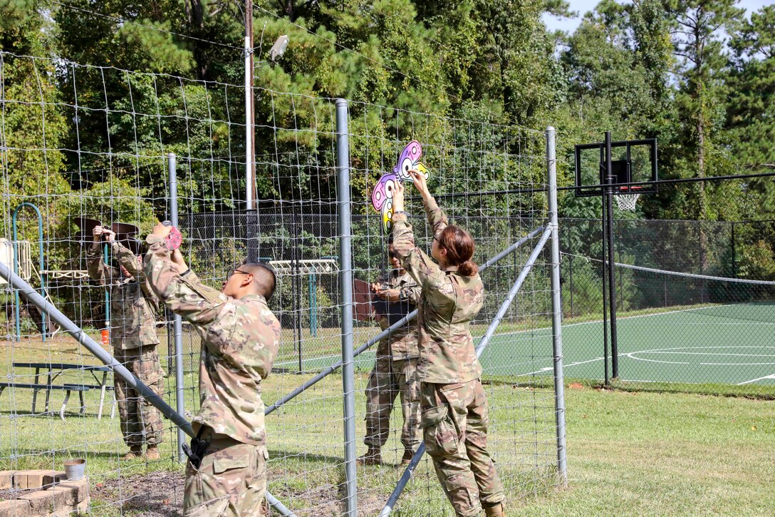 Soldiers put wooden butterflies onto a fence.